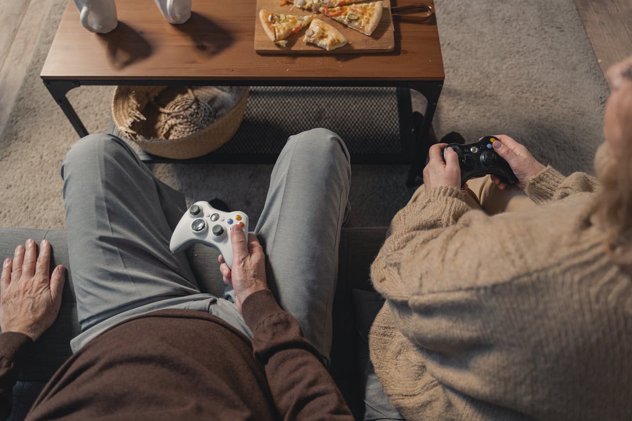 Elderly couple playing video games on the sofa, enjoying leisure time with a console.