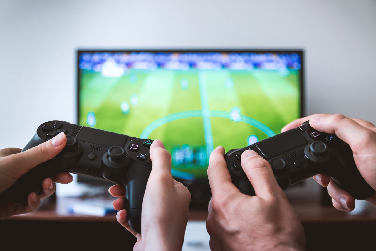 Close-up of hands holding gaming controllers in front of a TV. Engaged in a video gaming session.